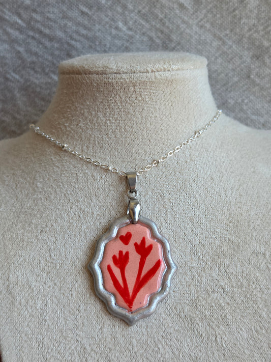 Medalla rosada y rojo con pátina plateada y cadena con baño de plata