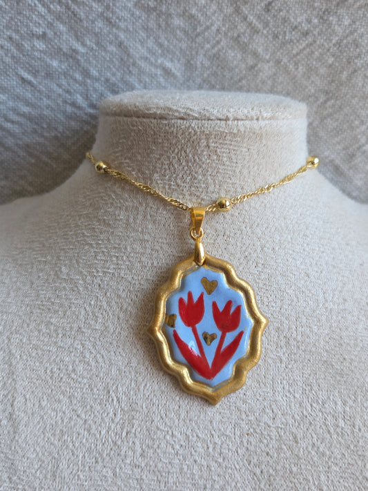 Medalla celeste y rojo con pátina dorada, detalles en oro y cadena con baño de oro